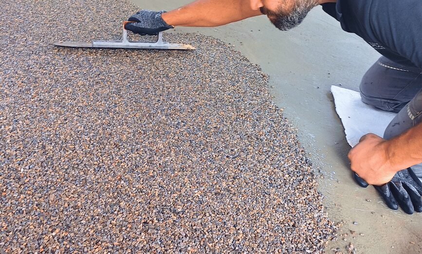 Kies Masse wird von einem SACO Haus und Garten Mitarbeiter sauber aufgezogen.